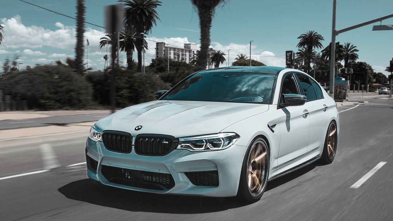 White BMW M5 on road with palm trees.