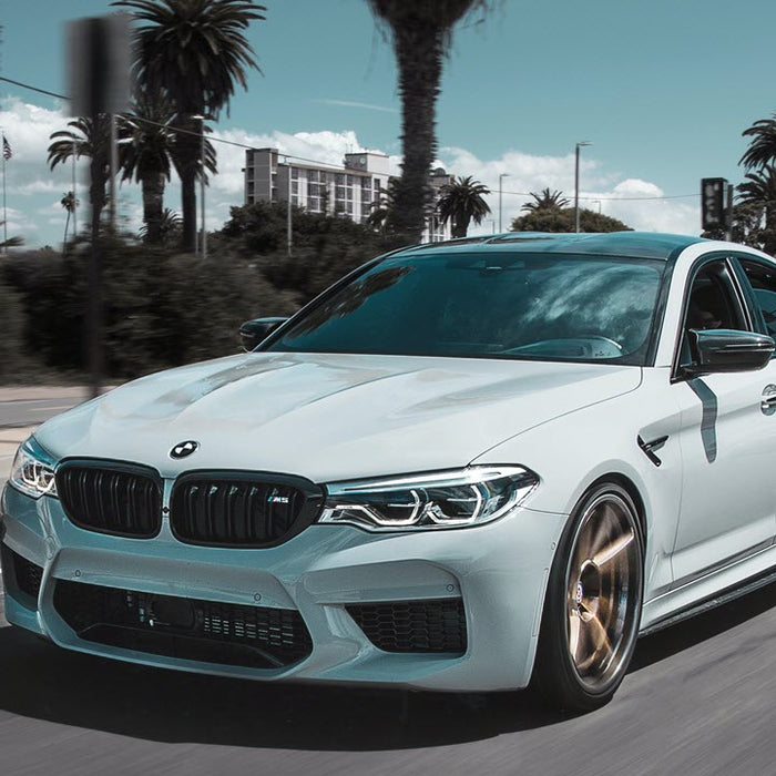 White BMW M5 on road with palm trees.
